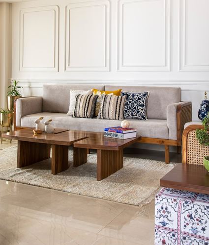 Living room with cane-and-wood sofa, patterned cushions, and geometric wooden coffee tables on a jute rug