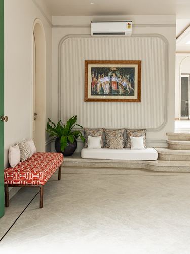 Foyer nook with built-in cushioned bench, framed artwork, and red patterned bench beside arched doorway