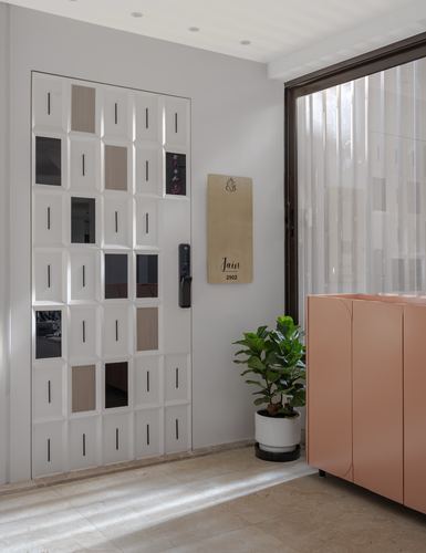 Entryway with geometric patterned door, wooden nameplate, potted plant, and pink cabinet by glass wall