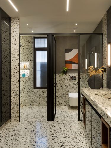 Terrazzo-clad bathroom with black steel glass partitions, floating vanity, and framed artwork niche.