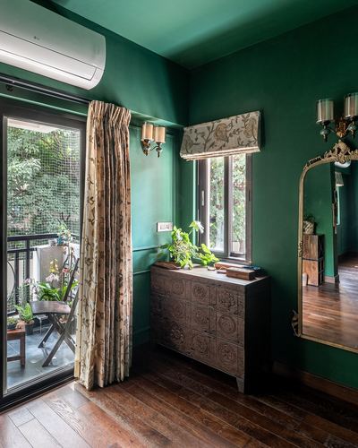 Deep green room with carved wooden chest, gold mirror, and floral curtains near balcony door
