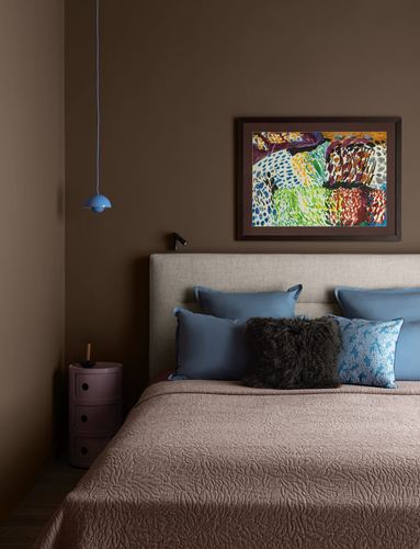 Brown bedroom with upholstered headboard, blue pillows, mauve bedspread and colorful framed artwork above
