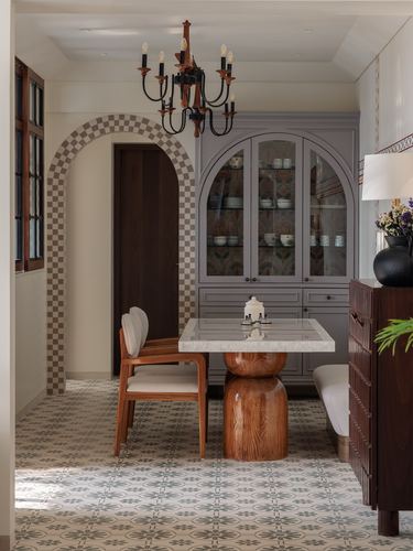 Dining nook with sculpted wood table, marble top, arched cabinet, and patterned floor tiles