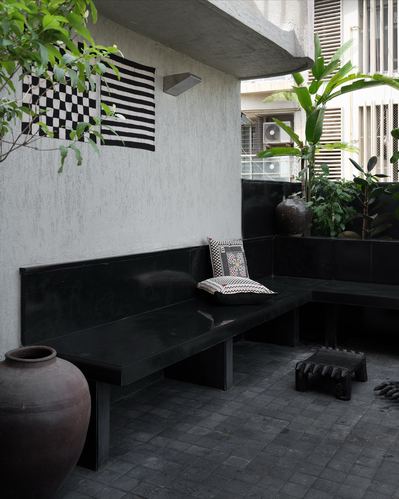 Corner balcony with black stone L-bench, terracotta pot, and checkered textile on textured grey wall