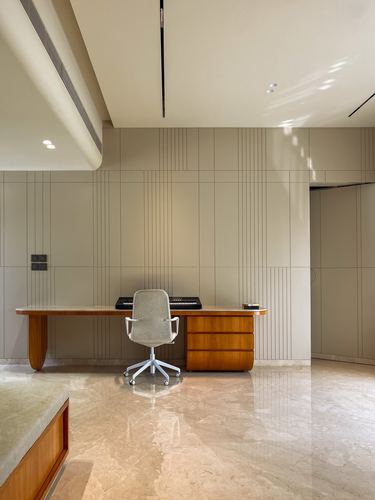 Minimalist study with curved wooden desk against grooved beige wall panel on polished stone floor