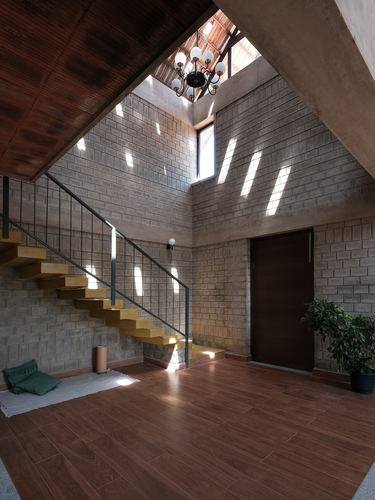 Double-height foyer with exposed block walls, wooden staircase, skylight casting light strips, dark wood door