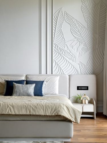 Bedroom with upholstered bed, blue pillows, and a carved leaf-pattern plaster wall panel.
