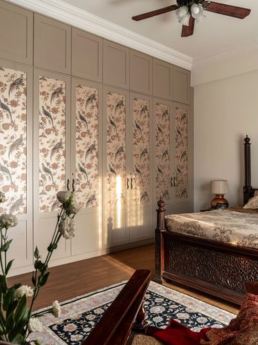 Bedroom with carved wooden four-poster bed and floral fabric-paneled wardrobe wall in warm afternoon light