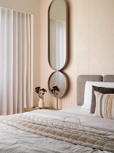 Beige bedroom with grey headboard, layered pillows, and a tall oval mirror above a bedside table