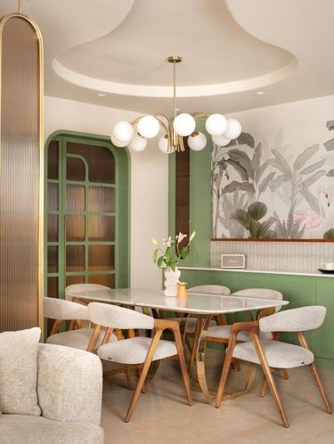 Dining room with sage-green arched cabinetry, marble table, wooden chairs, and flamingo mural wallpaper
