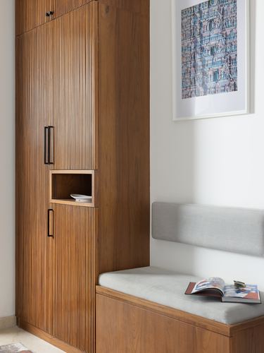 Slatted wood shoe cabinet beside a grey bench and framed artwork in an entryway