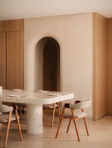 Terrazzo dining table with wooden chairs set before an arched niche in a beige plaster wall