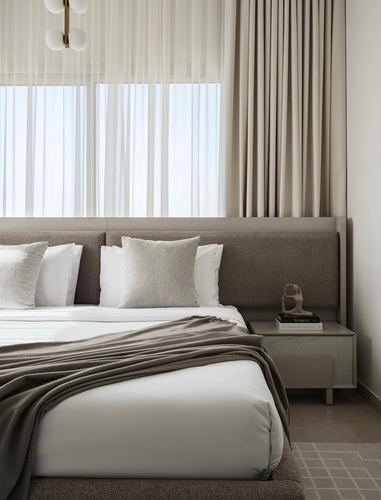 Neutral-toned bedroom with upholstered headboard, sheer curtains, and stone-topped nightstand