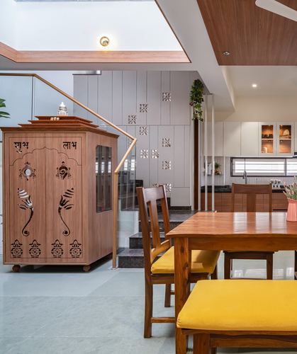 Wooden pooja cabinet beside staircase with dining table and yellow bench in open-plan home