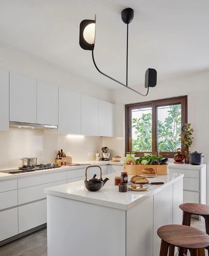 All-white kitchen with island, wooden stools, and sculptural black pendant lamp near window