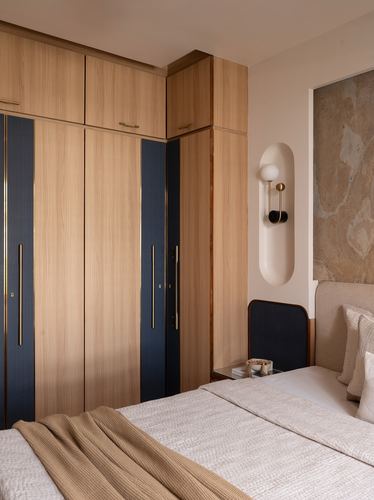 Wood wardrobe with navy fabric panels beside bed with stone-clad wall and sconce