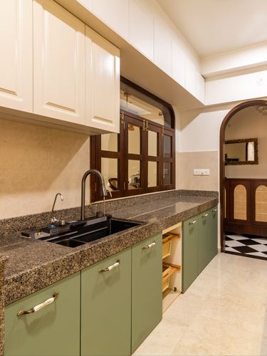 Olive-green kitchen cabinetry with granite countertop and arched wooden window opening to a passage