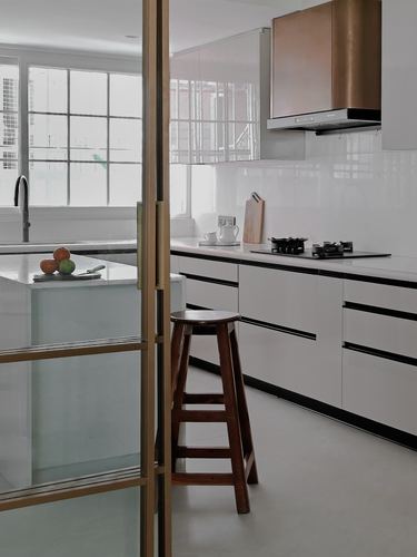 White modern kitchen with copper chimney hood, glass partition, and wooden bar stool