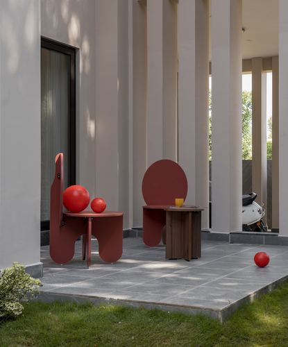 Red sculptural chairs and side table on grey stone patio beside fluted columns