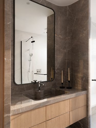 Bathroom vanity with veined stone wall, integrated stone sink, wood drawers, and mirror reflecting shower