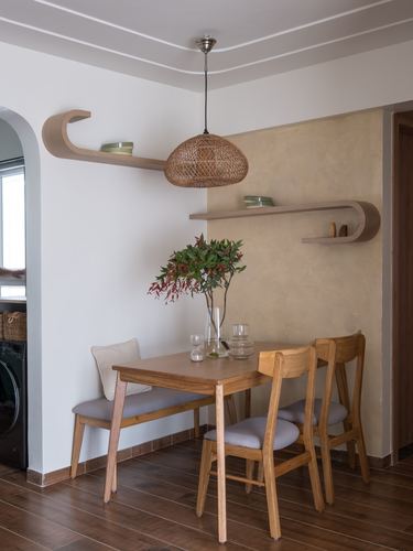 Dining nook with wooden table, bench, chairs, woven pendant light and curved corner shelves against warm plaster wall