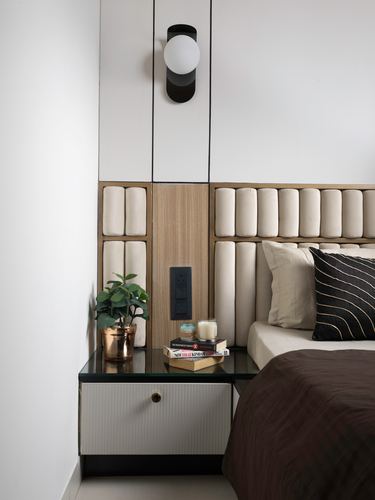 Beige tubular tufted headboard beside floating nightstand with plant and books, globe sconce above
