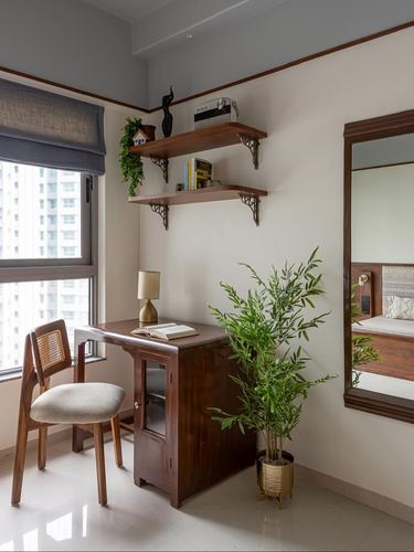 Small wooden study nook with cane chair, shelves, and mirror reflecting bedroom beyond