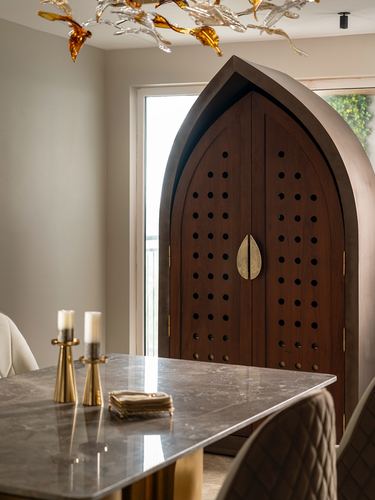 Arched wooden perforated cabinet with brass handle beside dining table with candlesticks