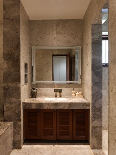 Marble-clad bathroom vanity with dark wood louvered cabinets and backlit mirror