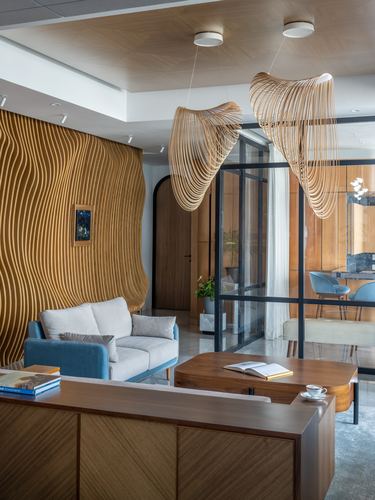Living room with wavy wood feature wall, sculptural pendant lights, and blue-grey sofa