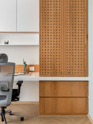 Home study nook with perforated wood cabinet, built-in white desk, and grey office chair