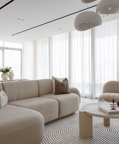 Beige living room with curved sofa, round stone coffee table, and floor-to-ceiling sheer curtains
