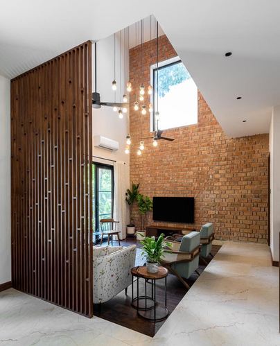 Double-height living room with exposed brick wall, wooden slat partition, and cluster pendant lights