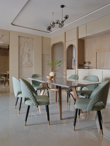 Dining room with sage velvet chairs, marble-top table, and carved buddha relief wall panel