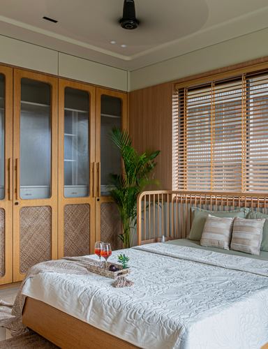 Wood-paneled bedroom with cane wardrobe, spindle headboard, wooden blinds and a bedside tray with drinks