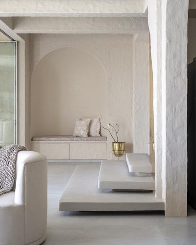 Minimalist beige living room with arched niche, window seat, and layered stone platform tables