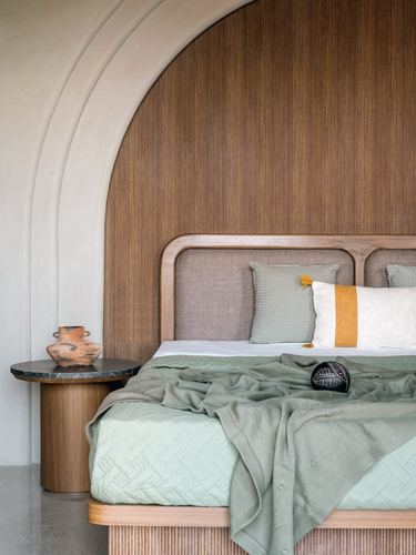 Bed against fluted wood panelled arch niche with sage throw and terracotta vase on side table