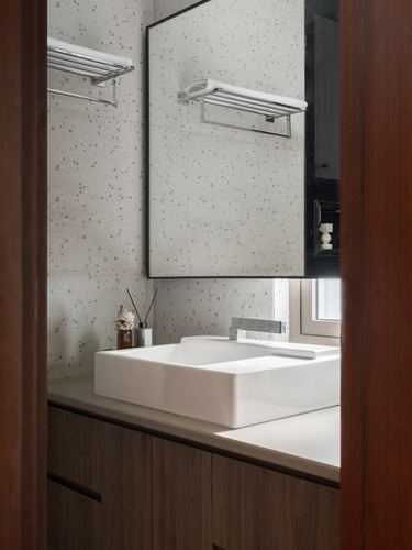 Bathroom vanity with rectangular sink and terrazzo wall seen through a dark wood door frame