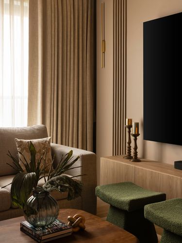 Living room corner with linen curtains, fluted panelling, wood console under tv, and green boucle stools