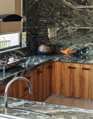 Kitchen counter and backsplash in green-veined stone with wood cabinetry, stove, and fruit basket