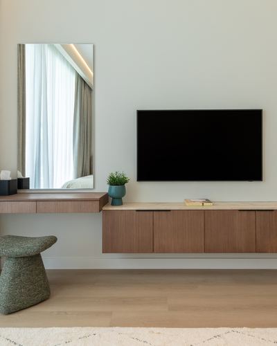 Floating wood console with mounted tv, mirror desk, and green stool on wood floor