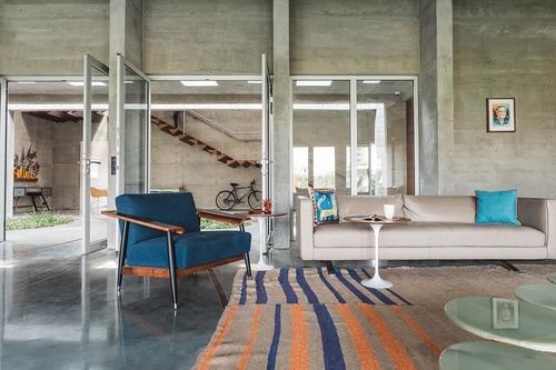 Living room with concrete columns, blue armchair, beige sofa, tulip tables and striped rug, glass doors open to courtyard