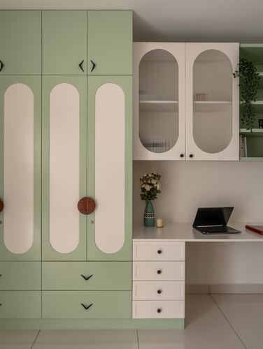 Sage green wardrobe with arched cream panels beside a white study desk and fluted glass cabinets