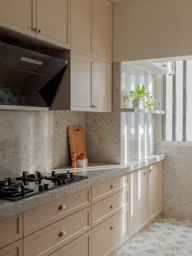 Blush pink galley kitchen with stone-look backsplash, black chimney hood, and sunlit window seat