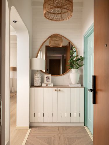 Entryway with round wood mirror, rattan pendant, white cabinet and open teal door