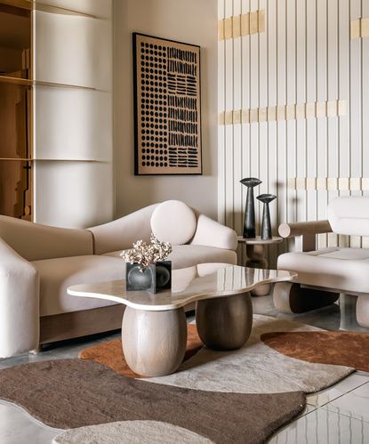 Beige living room with curved sofas, sculptural wood-and-stone coffee table, and fluted wall panelling