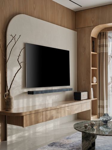 Wall-mounted tv on curved textured panel above floating wood console with arched shelving