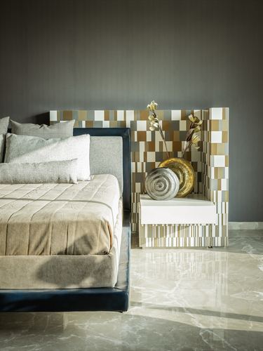 Bed with navy upholstered frame beside mosaic-tiled nightstand wall and gold vase on marble floor