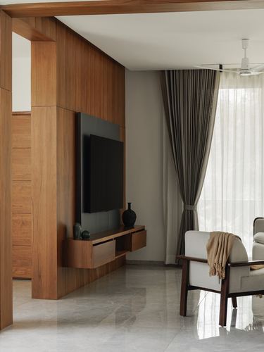 Wood-panelled living room corner with floating tv console, sheer curtains, and cane-armed chair