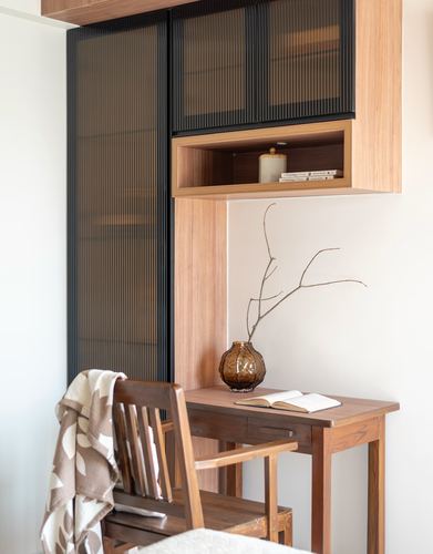 Small wooden study nook with chair, desk, open book and vase with dried branch